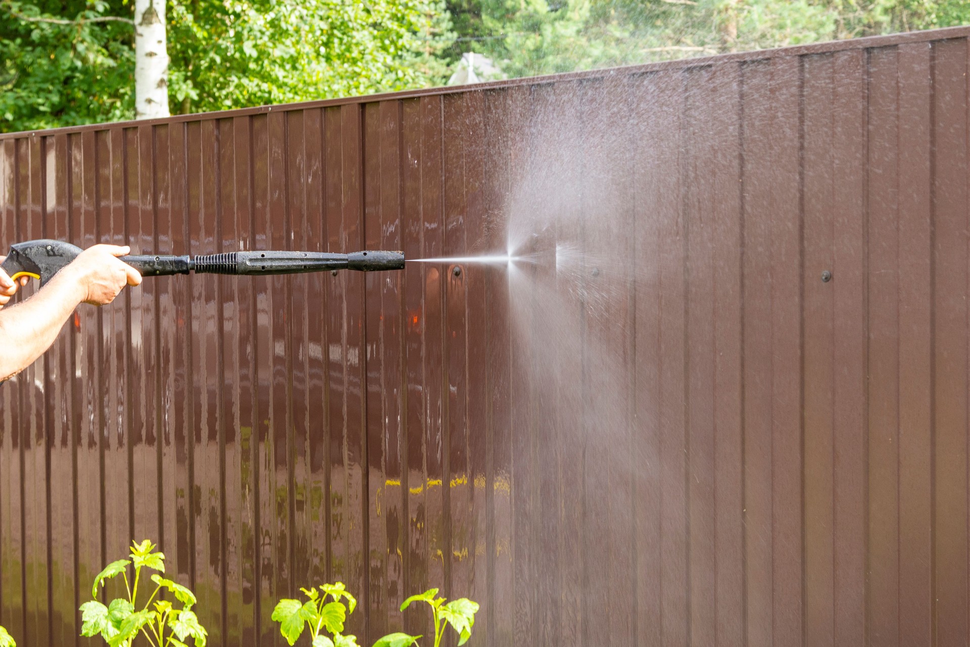 Cleaning fence with high pressure power washer, cleaning dirty wall.